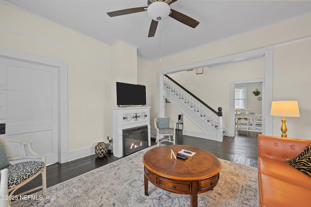 living area featuring stairway, wood finished floors, baseboards, ceiling fan, and a glass covered fireplace