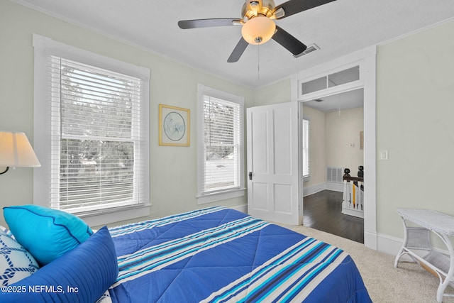 carpeted bedroom with visible vents, baseboards, ornamental molding, and a ceiling fan