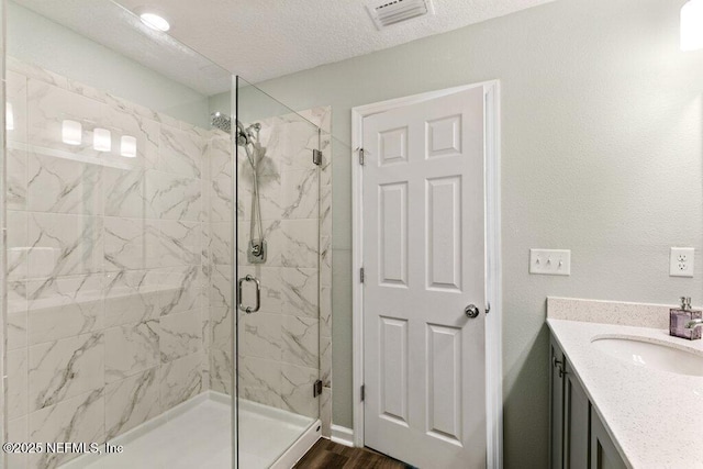 bathroom with a marble finish shower, visible vents, vanity, wood finished floors, and a textured ceiling