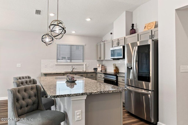 kitchen featuring visible vents, gray cabinets, tasteful backsplash, stainless steel appliances, and stone counters