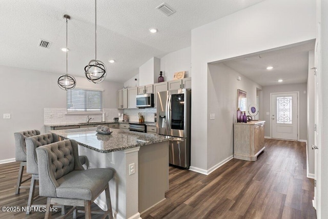 kitchen with visible vents, lofted ceiling, a kitchen island, and appliances with stainless steel finishes