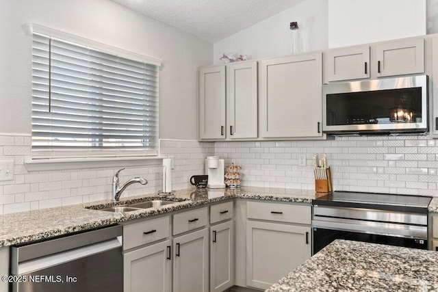 kitchen featuring lofted ceiling, a sink, appliances with stainless steel finishes, a textured ceiling, and tasteful backsplash