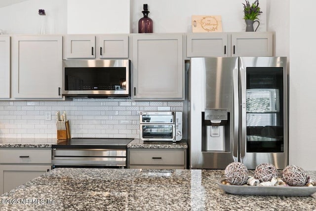 kitchen featuring decorative backsplash, dark stone countertops, a toaster, and appliances with stainless steel finishes