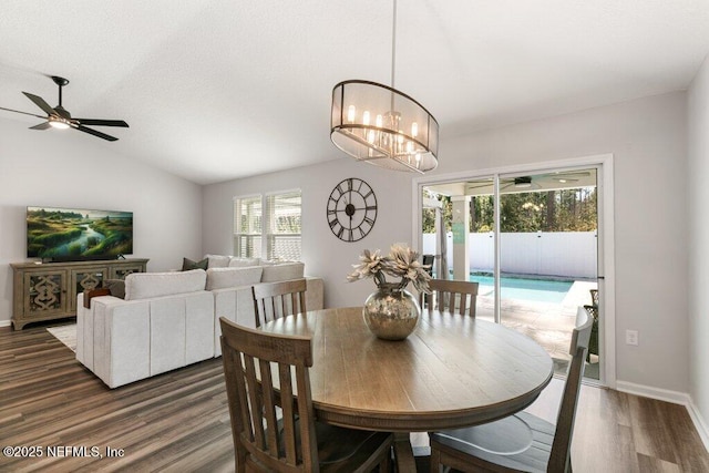 dining space featuring baseboards, ceiling fan with notable chandelier, dark wood-type flooring, and vaulted ceiling