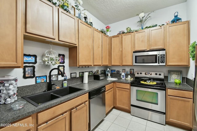 kitchen with light tile patterned floors, a sink, stainless steel appliances, a textured ceiling, and dark countertops