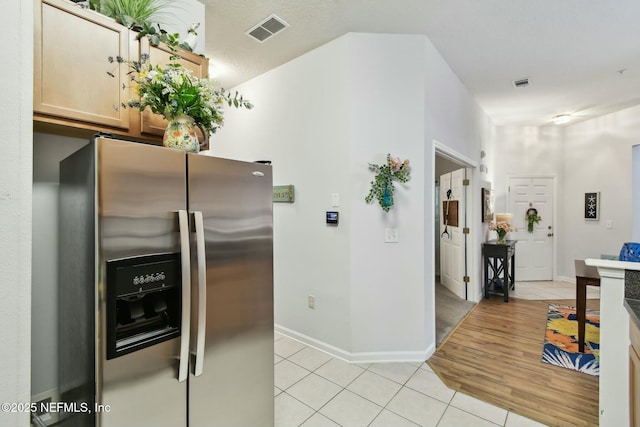 kitchen with light tile patterned floors, visible vents, stainless steel fridge, and baseboards