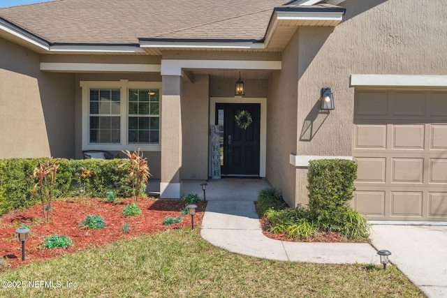 entrance to property featuring stucco siding, an attached garage, and a shingled roof