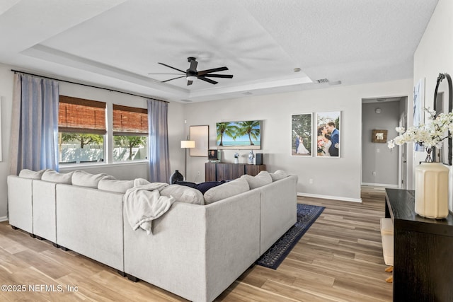 living room with light wood-style floors, baseboards, a raised ceiling, and a ceiling fan