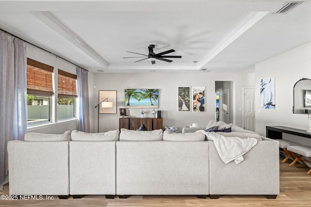 living area with visible vents, a ceiling fan, light wood-type flooring, and a tray ceiling