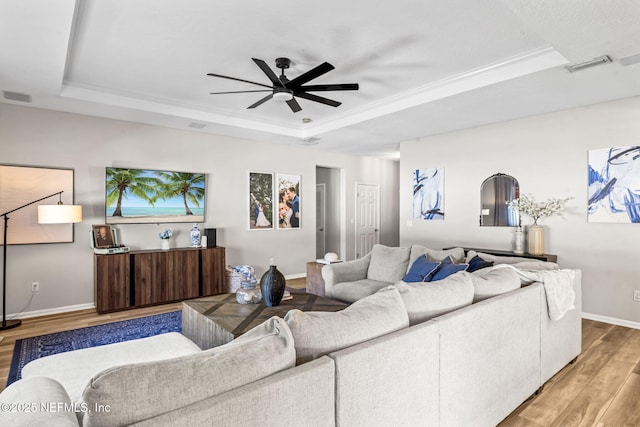 living room with baseboards, visible vents, a tray ceiling, ceiling fan, and light wood-type flooring