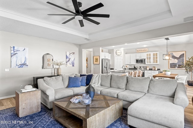 living room with a raised ceiling, wood finished floors, visible vents, and ceiling fan