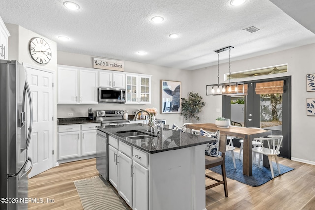 kitchen featuring a kitchen bar, visible vents, a sink, stainless steel appliances, and white cabinets