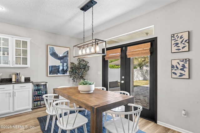 dining area with baseboards, wine cooler, light wood-type flooring, french doors, and a textured ceiling