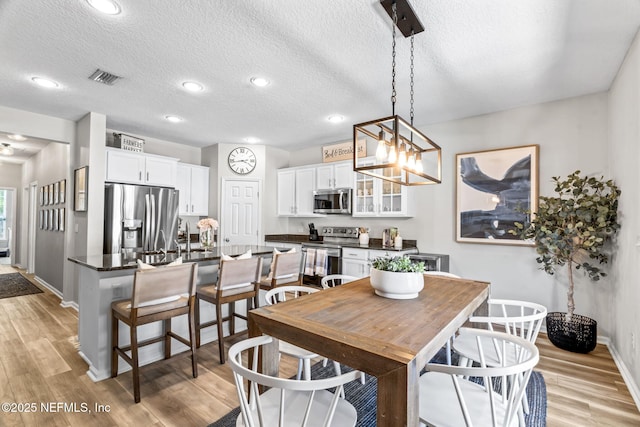 dining area with visible vents, a textured ceiling, recessed lighting, light wood-style floors, and baseboards