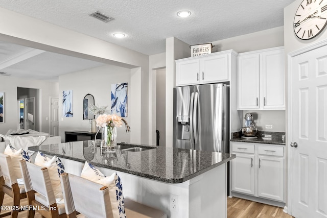 kitchen with light wood-type flooring, a sink, white cabinetry, dark stone counters, and stainless steel fridge