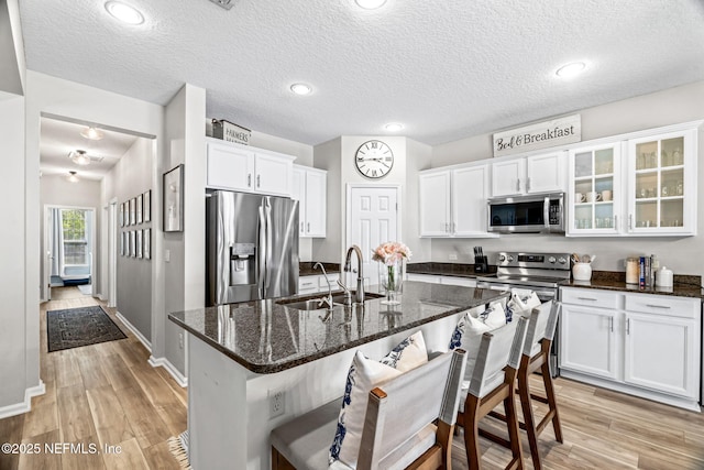 kitchen featuring a sink, a kitchen breakfast bar, white cabinetry, stainless steel appliances, and light wood finished floors