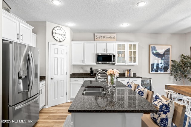 kitchen with an island with sink, light wood-type flooring, appliances with stainless steel finishes, white cabinetry, and a sink