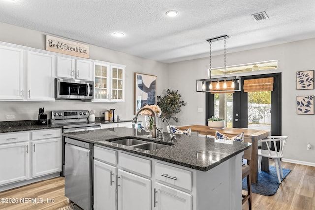 kitchen featuring a sink, stainless steel appliances, a kitchen island with sink, and white cabinetry