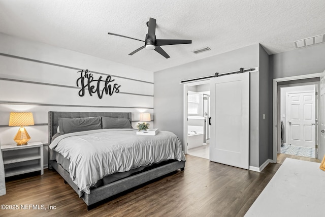 bedroom with a barn door, a textured ceiling, visible vents, and dark wood-style floors