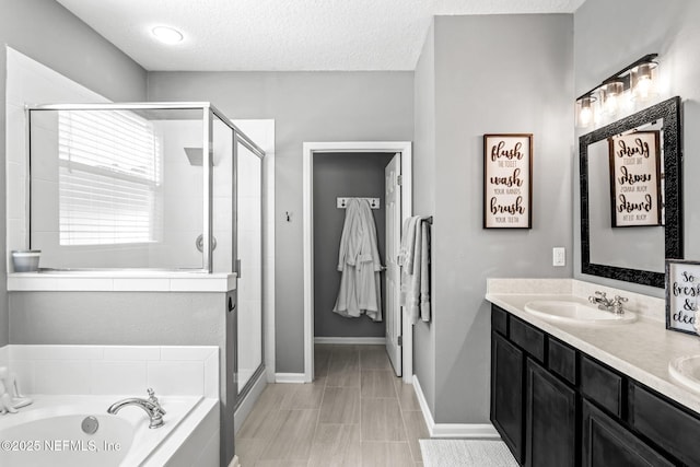 full bathroom with a garden tub, a sink, a textured ceiling, a shower stall, and double vanity