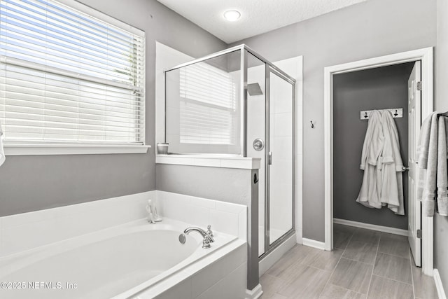 full bath featuring a bath, a stall shower, a textured ceiling, and baseboards