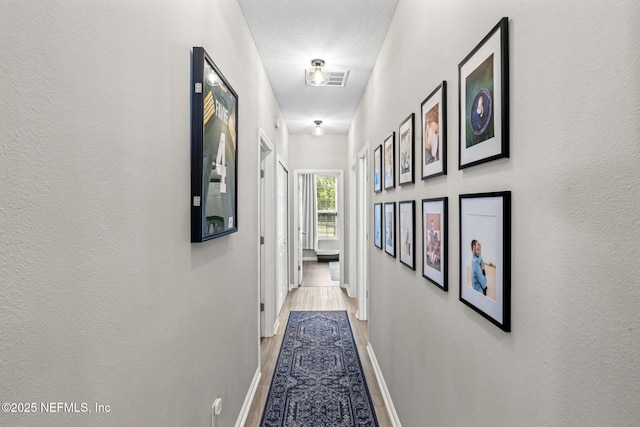 hallway with visible vents, baseboards, wood finished floors, and a textured wall