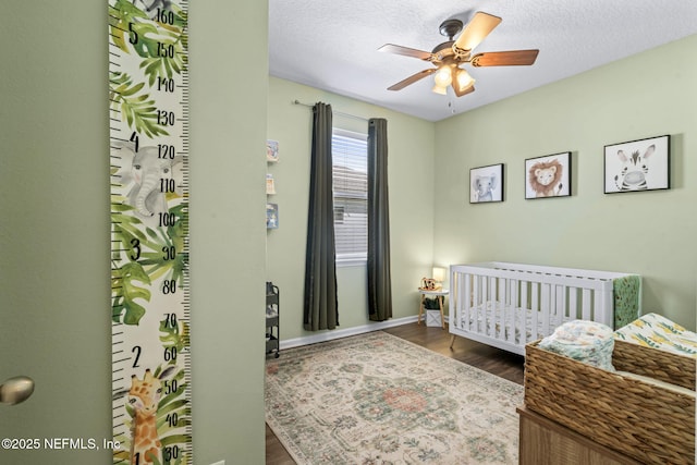 bedroom with a nursery area, wood finished floors, a ceiling fan, and a textured ceiling