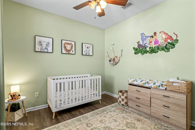 bedroom featuring visible vents, baseboards, a nursery area, and wood finished floors