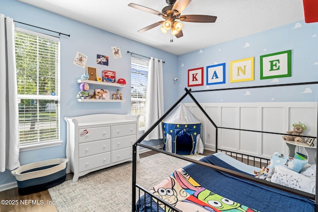 bedroom featuring a textured ceiling, multiple windows, wood finished floors, and wainscoting