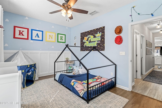 bedroom with visible vents, wood finished floors, wainscoting, and a decorative wall