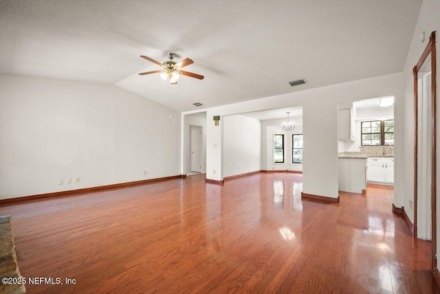 unfurnished living room featuring visible vents, baseboards, light wood-type flooring, lofted ceiling, and ceiling fan with notable chandelier