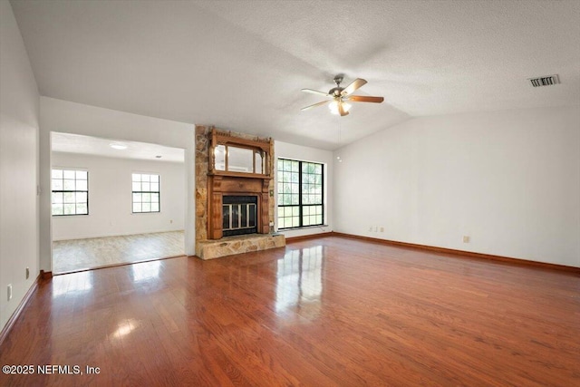 unfurnished living room with wood finished floors, visible vents, lofted ceiling, ceiling fan, and a large fireplace