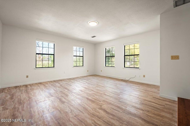 unfurnished room with light wood finished floors, visible vents, a textured ceiling, and baseboards