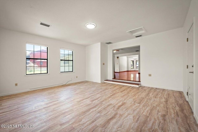 unfurnished room with baseboards, visible vents, attic access, and light wood-style floors