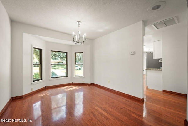 unfurnished room featuring a notable chandelier, baseboards, a textured ceiling, and light wood finished floors