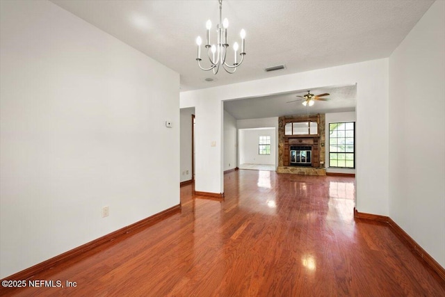 unfurnished living room featuring visible vents, baseboards, ceiling fan with notable chandelier, wood finished floors, and a textured ceiling