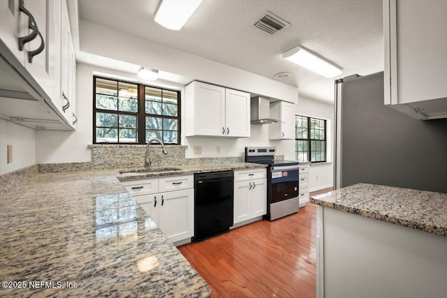 kitchen featuring visible vents, wall chimney range hood, stainless steel appliances, white cabinetry, and a sink