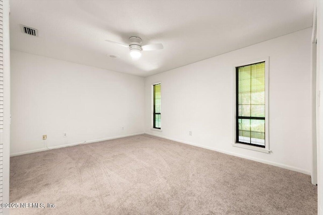 carpeted empty room with visible vents, baseboards, a healthy amount of sunlight, and a ceiling fan