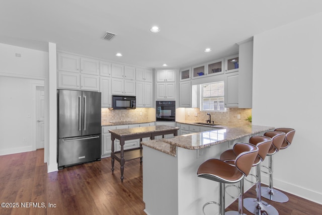 kitchen featuring tasteful backsplash, a peninsula, black appliances, visible vents, and a sink