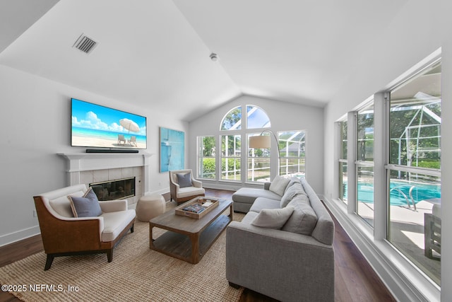 living room with visible vents, baseboards, wood finished floors, a tile fireplace, and lofted ceiling