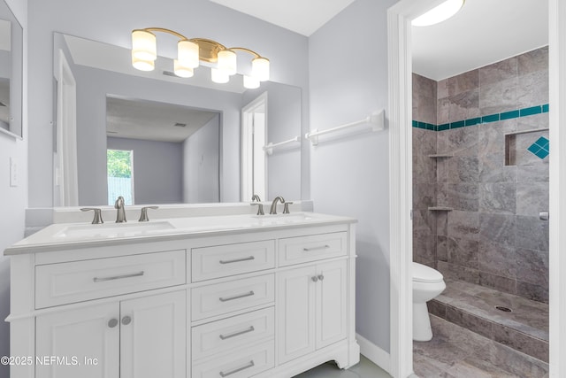 full bathroom featuring double vanity, toilet, tiled shower, and a sink