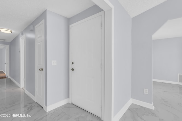 hallway featuring marble finish floor, a textured ceiling, and baseboards