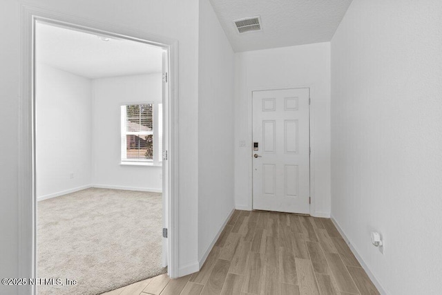 hall featuring visible vents, baseboards, light wood-style floors, and a textured ceiling