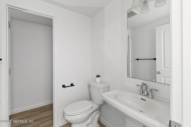 half bath with visible vents, baseboards, wood finish floors, toilet, and a sink