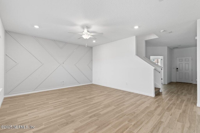 empty room with stairway, a ceiling fan, light wood-style flooring, recessed lighting, and a textured ceiling