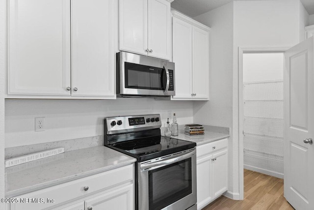 kitchen featuring white cabinetry, light stone countertops, light wood-style floors, and appliances with stainless steel finishes