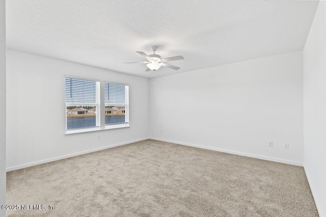 carpeted spare room featuring baseboards, a textured ceiling, and ceiling fan