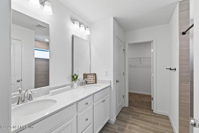 bathroom with a textured ceiling, wood tiled floor, visible vents, and a sink