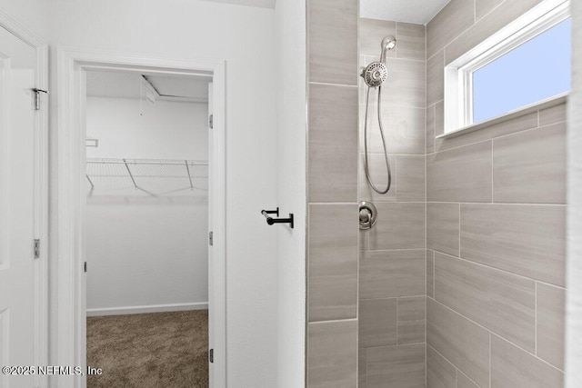 full bathroom featuring a spacious closet, baseboards, and a tile shower