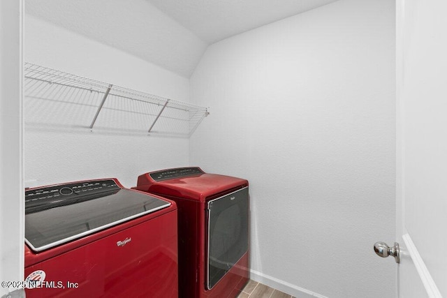 clothes washing area with baseboards, wood finished floors, laundry area, and washer and clothes dryer